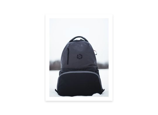 Mockup of a backpack sitting in snow that has the logomark printed on it